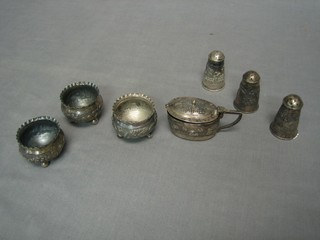 An Eastern embossed white metal 7 piece condiment set comprising mustard pot, 3 pepper pots and 3 salts