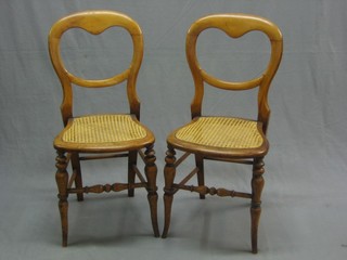A pair of Victorian bleached mahogany balloon back bedroom chairs with woven cane seats, raised on turned supports