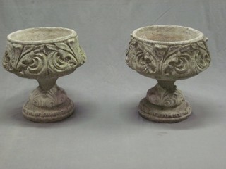 A circular pair of well weathered concrete garden urns raised on spreading feet