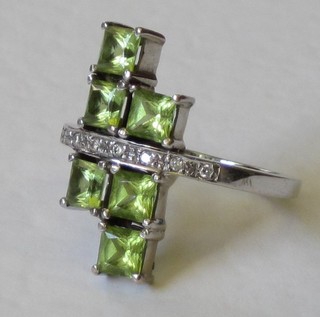 A lady's 18ct white gold dress ring set 6 square cut peridots, supported by diamonds