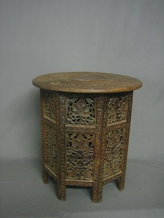 A circular Indian hardwood table with carved floral decoration, raised on a folding stand 20"