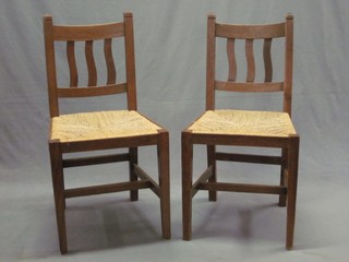 A set of 6 oak Arts and Crafts stick and rail back dining chairs with woven rush seats, raised on square tapering supports
