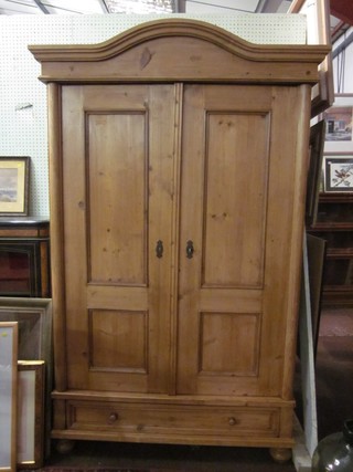 A Continental stripped and polished pine wardrobe with domed cornice, the interior fitted a hanging rail and shelves enclosed by a panelled door, the base fitted 1 long drawer 47"