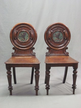 A pair of 19th Century mahogany hall chairs with painted armorial backs and solid seats, raised on turned supports