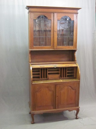 A Victorian Art Nouveau honey oak cylinder bureau bookcase, the upper section with moulded cornice, the interior  fitted shelves enclosed by lead glazed panelled doors above recess, the base with fall front enclosed by a tambour shutter above a cupboard enclosed by arched panelled door, raised on cabriole supports 36"