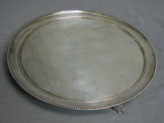 A circular silver plated salver with bead work border, raised on 3 panelled supports 11"