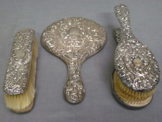 A 5 piece embossed silver backed dressing table set with hand mirror, pair of hair brushes, pair of clothes brushes, heavily dented