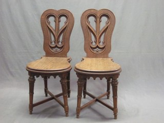 A pair of Victorian Continental oak hall chairs with pierced shaped backs, raised on turned supports with X framed stretchers