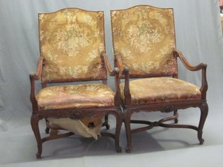 A pair of Continental walnut open arm chairs with upholstered seats and backs raised on cabriole supports with X framed stretcher