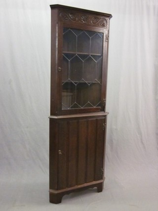 A carved oak double corner cabinet, the upper section fitted shelves enclosed by lead glazed panelled doors, the base fitted a cupboard enclosed by a panelled door 26"