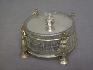 A circular cut glass butter dish contained in a silver plated frame decorated milk maids