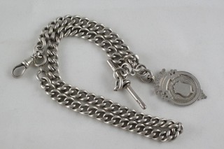 A silver curb link watch chain hung a silver medallion