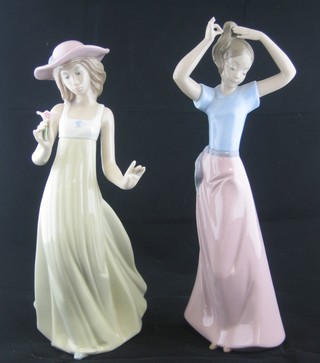 A Nao figure of a lady with hat admiring a bloom 10" and 1 other of a lady tying hair 10" (finger f)