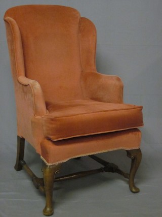 A Queen Anne style walnut winged armchair upholstered in rose pink Dralon and raised on cabriole supports