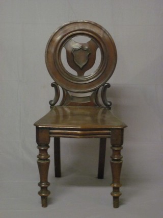 A Victorian mahogany solid seat hall chair with circular shield back and pierced decoration, raised on turned supports