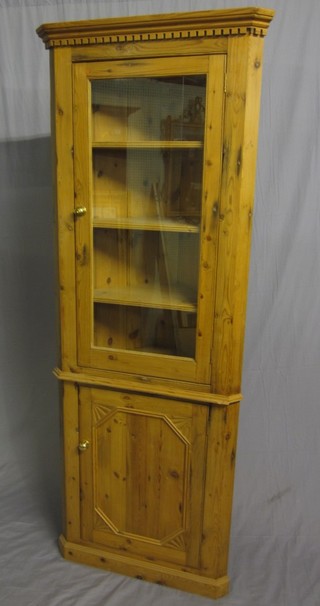 A 19th/20th Century pine double corner cabinet with moulded and dentil cornice, the interior fitted shelves enclosed by a glazed panelled door 29"