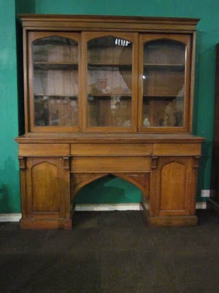 A Victorian Gothic honey oak bookcase on cabinet, the upper section with moulded cornice fitted shelves enclosed by arched panelled glazed sliding doors, the base fitted 2 long drawers and flanked by 2 cupboards 72"