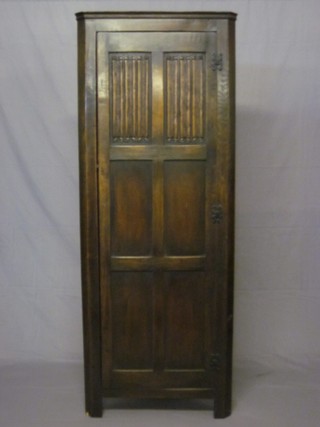 An oak corner hall wardrobe enclosed by a panelled door with linen fold decoration