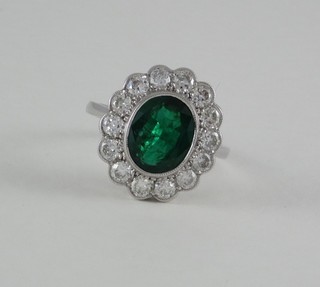 A lady's particularly attractive 18ct white gold dress ring set an oval cut emerald surrounded by numerous diamonds, approx 1.25/3.20ct