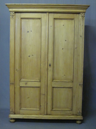 A Continental stripped and polished pine cupboard with moulded cornice, the interior fitted shelves enclosed by a pair of panelled  doors, raised on bun feet 48"