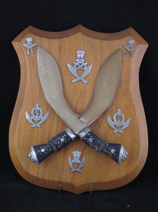 A wooden plaque with 2 decorative Kukris and various Gurkha  Regt. cap badges including Medical Service etc