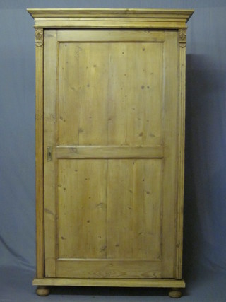 A Continental stripped and polished pine cupboard with moulded cornice, fitted adjustable shelves and enclosed by a single  panelled door with columns to the sides, raised on bun feet 43"