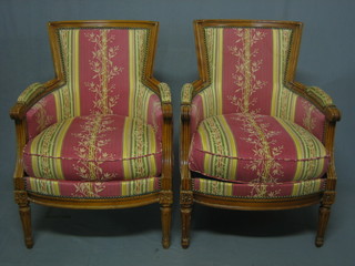 A pair of mahogany show frame armchairs upholstered in striped material, raised on turned and fluted supports
