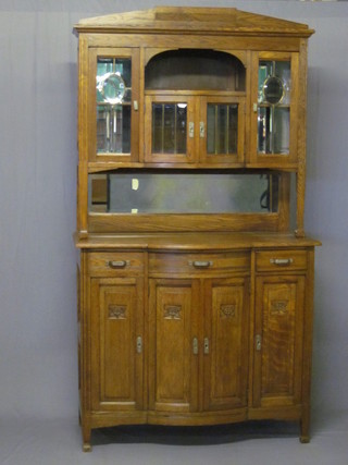 An Art Nouveau Continental oak bow front dresser, the raised  upper section fitted a recess above a cupboard flanked by a pair  of cupboards enclosed by glazed panelled doors above a recess,  the base fitted 1 long drawer flanked by 2 short drawers with  triple cupboard beneath 46"