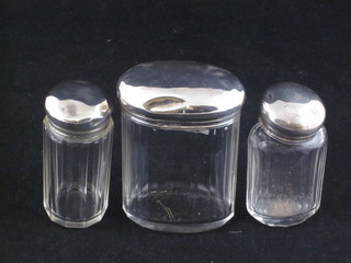 An oval glass pin jar with silver lid and 2 circular pin jars with silver lids