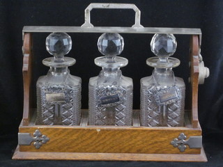 An oak and silver plated tantalus with 3 cut glass decanters together with silver plated labels ILLUSTRATED