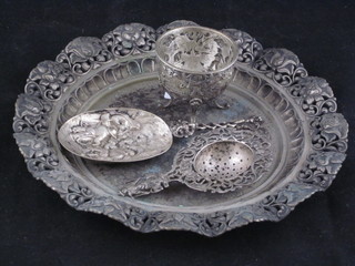 An Eastern embossed white metal circular dish, tea strainer, an embossed spoon decorated a dental scene and an embossed vase