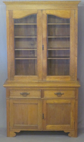 An Art Nouveau honey oak bookcase on cabinet, the upper  section with moulded cornice, the interior fitted adjustable  shelves enclosed by glazed panelled doors, the base fitted 2 short  drawers above a double cupboard, raised on bracket feet 48"