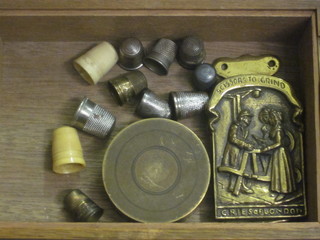 A wooden cigarette box with hinged lid containing a cylindrical brass trinket box, a brass pot and a collection of thimbles