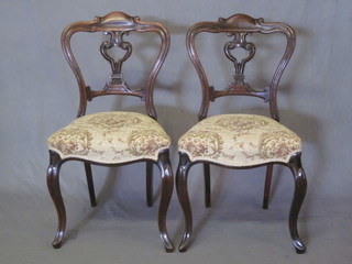 A set of 4 Victorian rosewood balloon back dining chairs with shaped slats to the middle, the seats of serpentine outline, raised  on cabriole supports