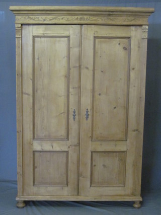 A Continental stripped and polished pine cabinet with moulded cornice, the shelved interior enclosed by panelled doors, raised  on bun feet 49"