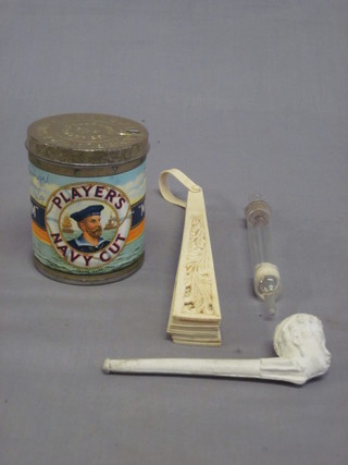 A tin of Players medium cut cigarettes marked Portugal May  1949, a clay pipe the bowl decorated a head, a glass syringe and  a fan