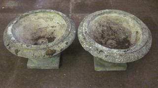 A pair of well weathered circular concrete garden urns with lobed borders, raised on square bases 23"