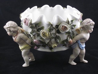 A Dresden style circular porcelain bowl with floral encrusted decoration supported by cherubs 7", f and r,