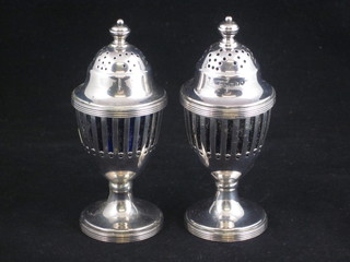 A pair of Georgian style pierced silver pepperettes, London 1906 with blue glass liners, raised on circular spreading feet, 3 ozs