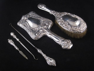 An embossed silver backed hand mirror, a similar hair brush, 2 silver handled button hooks and a nail file