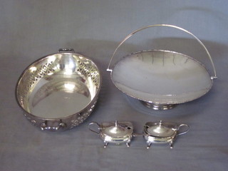 An oval pierced silver plated twin handled bowl, a circular cake basket with swing handle and 2 silver plated pepper pots