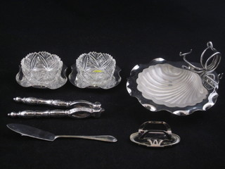 A silver scallop shaped butter dish, a pair of circular glass salts raised on a silver base and a pair of silver nut crackers