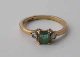 An 18ct yellow gold dress ring set a square cut emerald  supported by 2 diamonds