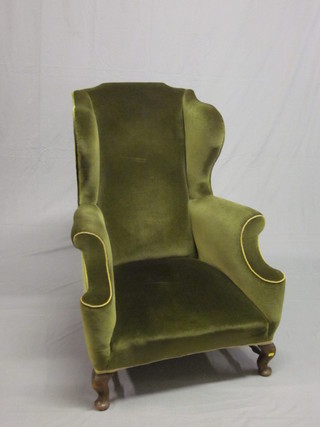A mahogany framed winged armchair upholstered in green  material, raised on cabriole supports with H framed stretcher