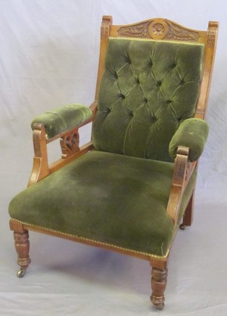 An Edwardian carved walnut open arm chair upholstered in green buttoned material, raised on turned supports