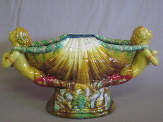 A Majolica style pottery twin handled urn of scallop form  supported by cherubs 21"