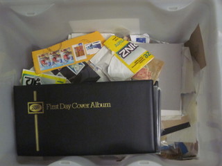 A plastic container containing an album of first day covers and various loose stamps etc