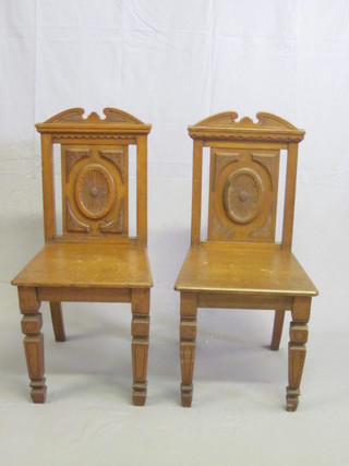 A pair of Victorian carved honey oak hall chairs with solid seats and backs, raised on square supports