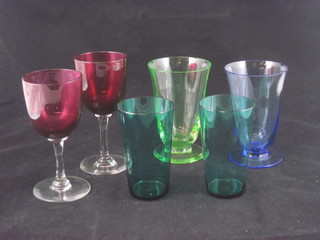 A pair of cranberry glass wine glasses with clear glass stems, 2 green glass beakers and 2 other beakers