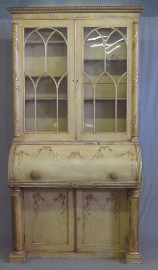 A 19th Century cream painted cylinder bureau, the upper section  with moulded cornice, the shelved interior enclosed by astragal  glazed doors, the cylinder front revealing a well fitted interior  above cupboards enclosed by panelled doors, raised on columns  45"  ILLUSTRATED